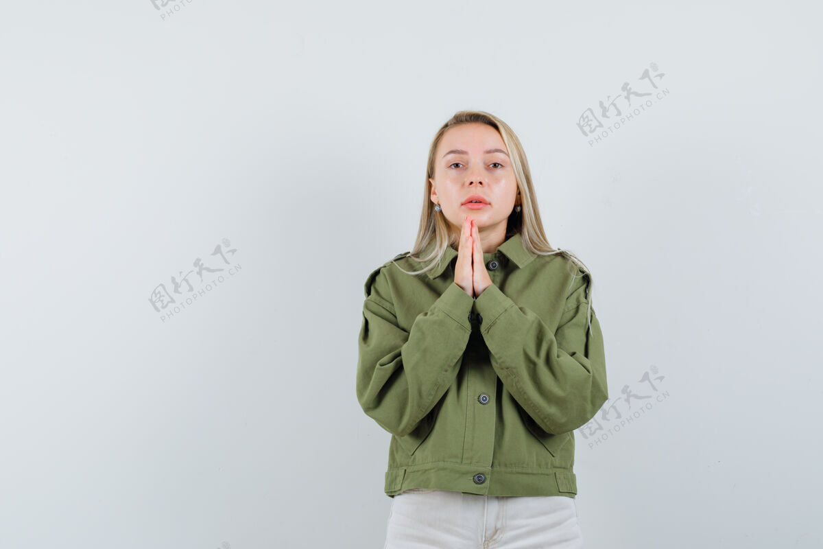 头发年轻的女性穿着绿色夹克 牛仔裤祈祷 看起来不耐烦 前视图自然封闭眼睛