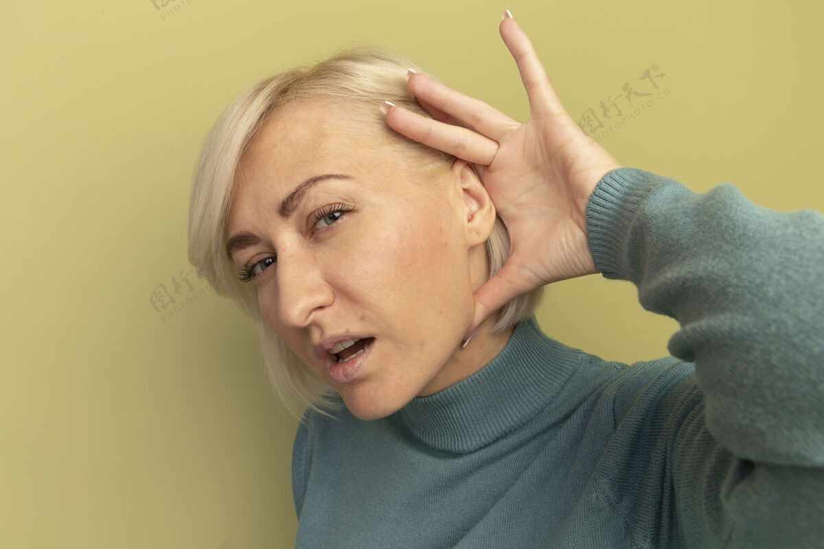 脸无知的美丽金发斯拉夫女人把手放在耳朵后面 隔离在橄榄绿的墙上斯拉夫拿着人