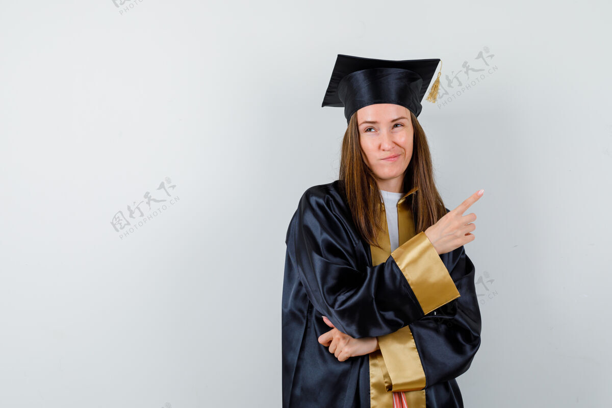 时尚年轻的女毕业生穿着学院服指着右上角 看起来很不高兴前视图微笑右人