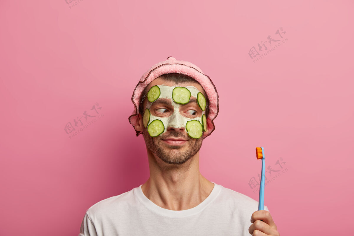 墙壁帅哥涂上泥面膜和新鲜黄瓜 看着牙刷 家里有早上的程序应用光滑帽子