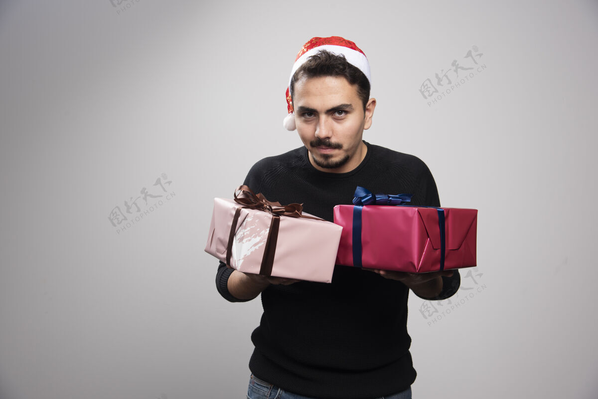 模特一个戴着圣诞老人帽子的笑脸男人 手里拿着新年礼物胡须蝴蝶结毛衣