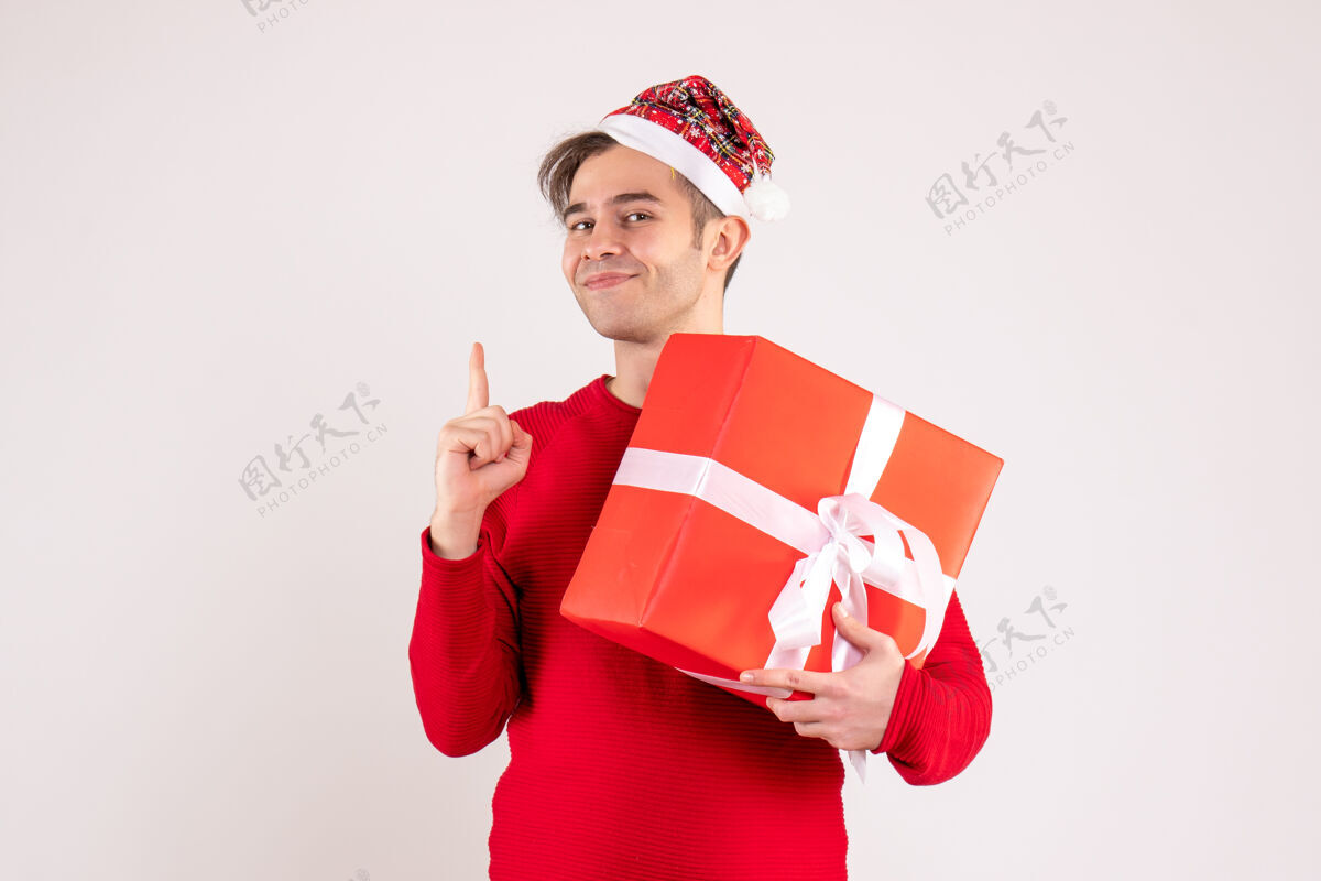 微笑正面图：戴着圣诞帽的年轻人手指在白色背景上人年轻人礼物