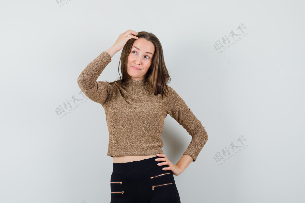 裤子年轻女子穿着金色的镀金毛衣和黑色的裤子 一只手放在腰上 另一只手放在脑后 看起来很迷人 前视图另一个年轻女性