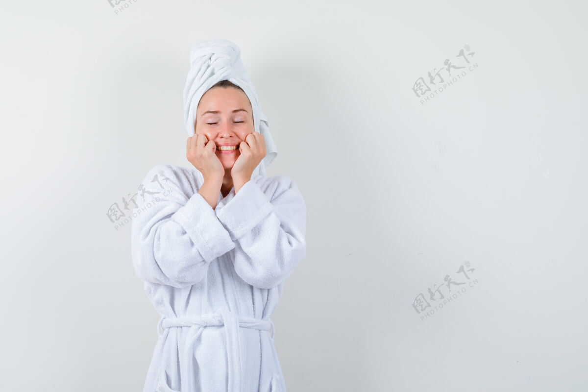 毛巾身穿白色浴袍的年轻女子 手放在面颊上 脸上挂着毛巾 看上去很快乐 正前方的景色漂亮保持微笑