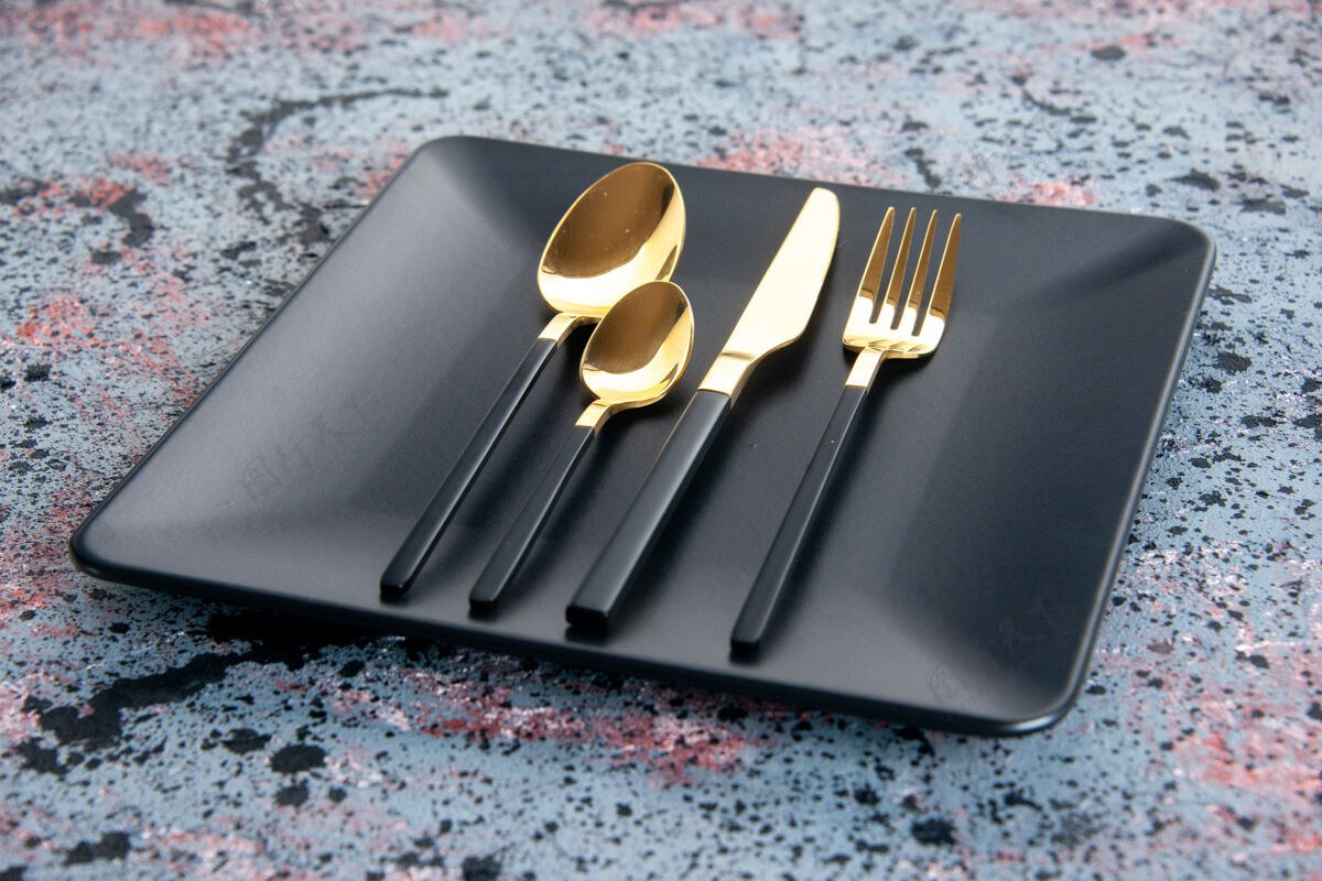 黑色盘子正面图黑色盘子 金色叉子 勺子和小刀 背景光线明亮深色晚餐托盘