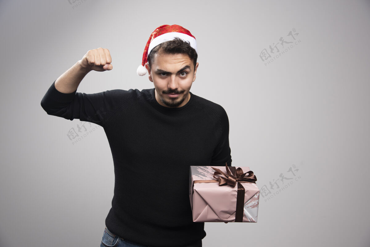 男性一个戴着圣诞老人帽子的年轻人展示着他的肌肉 手里拿着礼物礼物年份圣诞老人