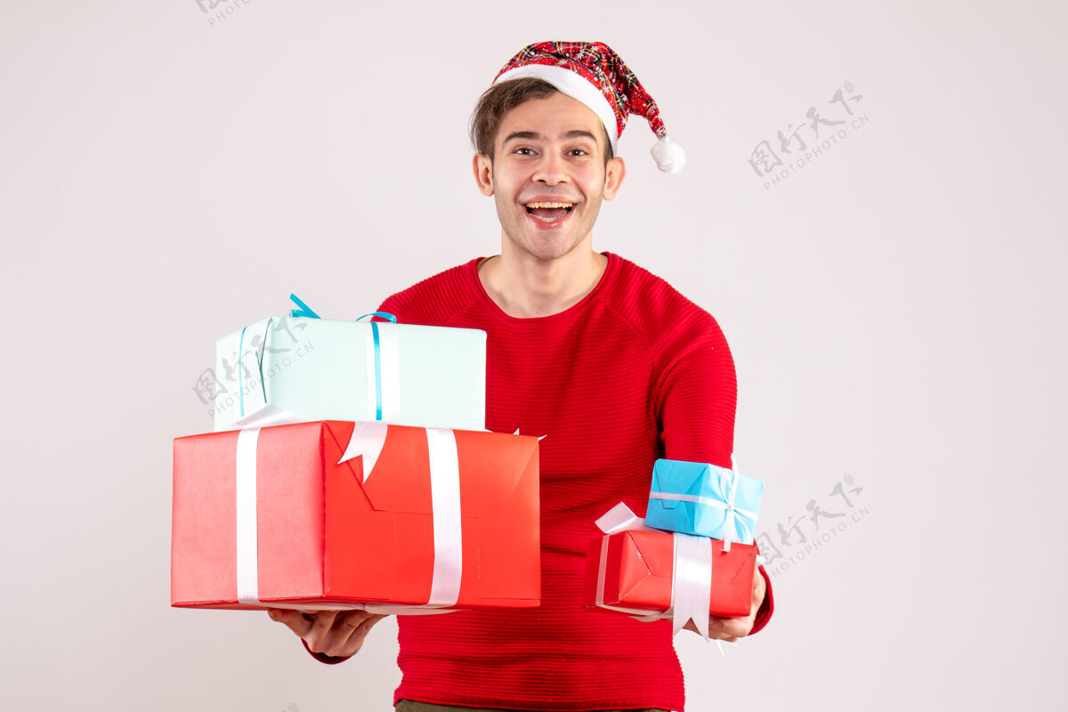 冬天前视图：戴着圣诞帽的年轻人拿着白色背景上的礼物前面圣诞节人