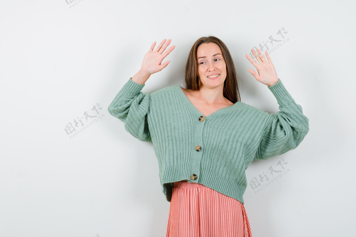 时尚年轻女孩举手投降的姿态在针织衫 裙子和看起来诱人前视图女性手掌快乐