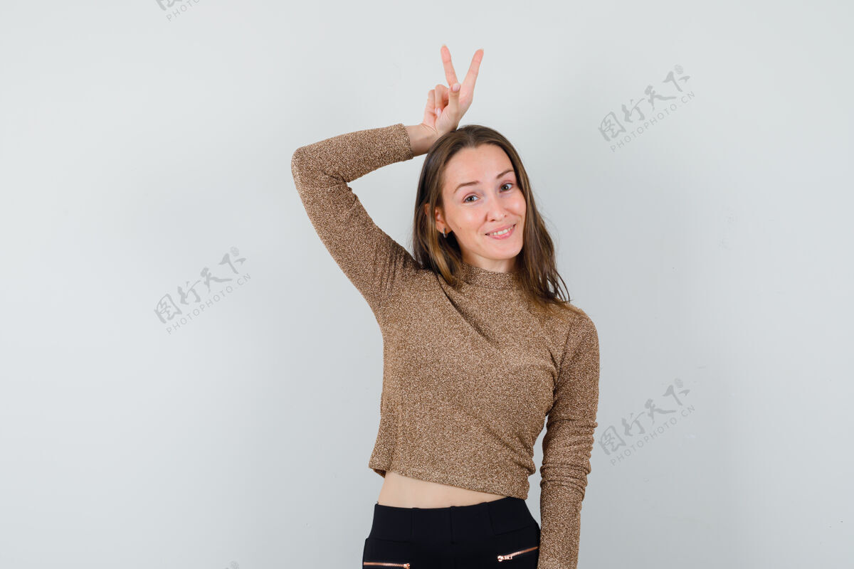 手势年轻女子举手表示 在金色镀金毛衣和黑色裤子兔子的姿态 看起来很有趣前视图手显示女孩