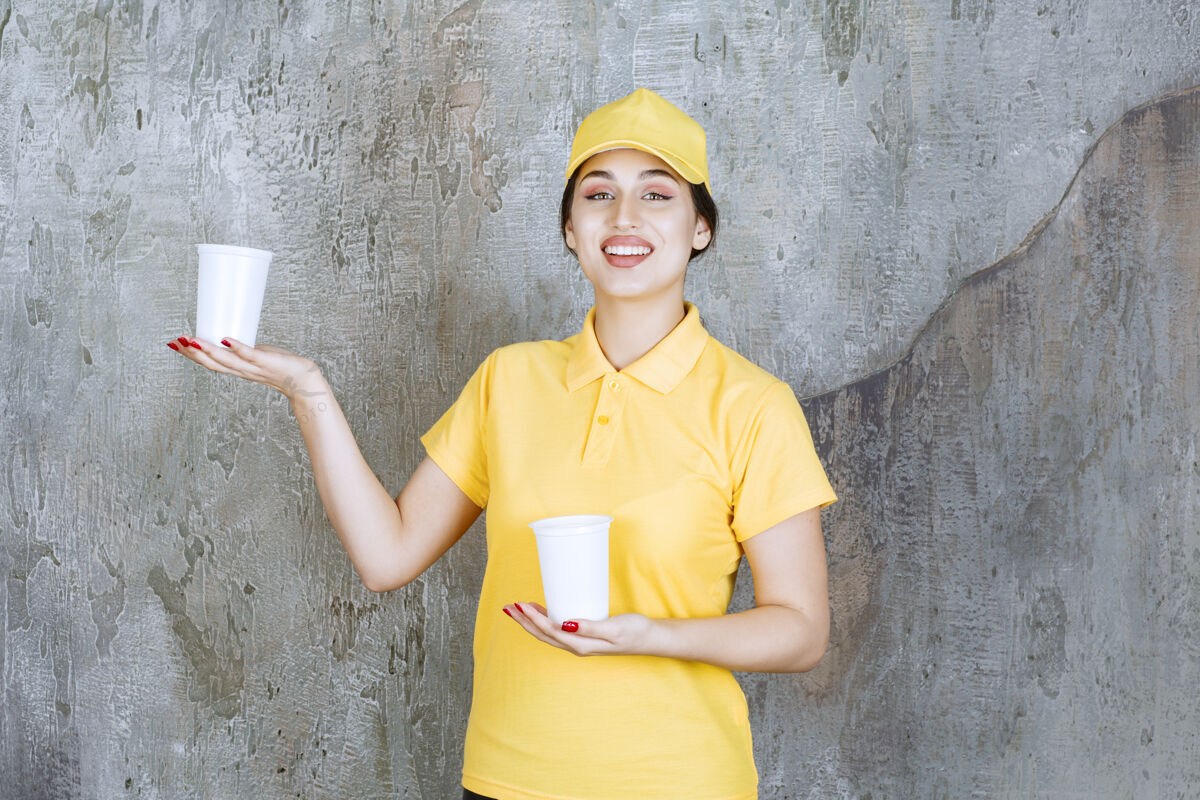 塑料一个穿着黄色制服的女送货员手里拿着两个塑料杯饮料 给另一个人一杯选择姿势女人