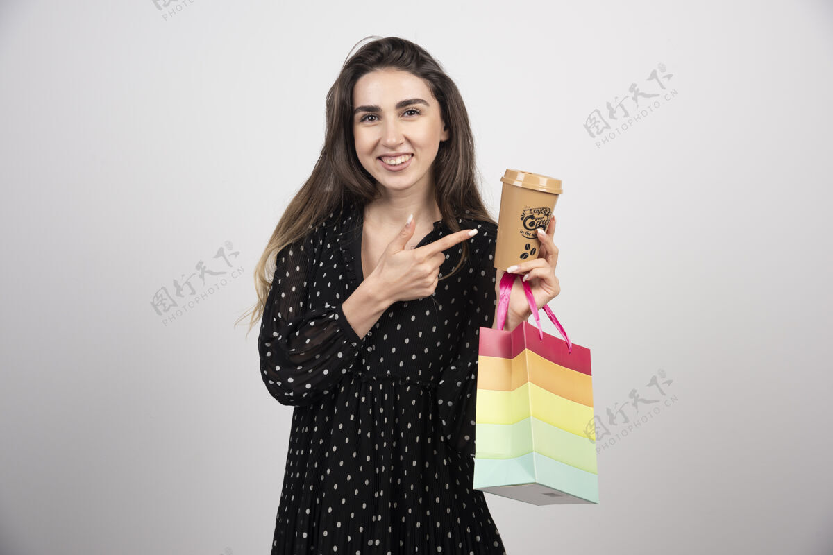 包年轻的女模特指着咖啡杯 手里拿着购物袋模特咖啡女性