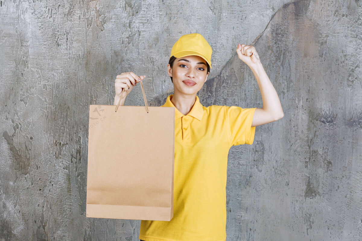快递身着黄色制服的女服务人员手持购物袋 并显示积极的手势送货成人人