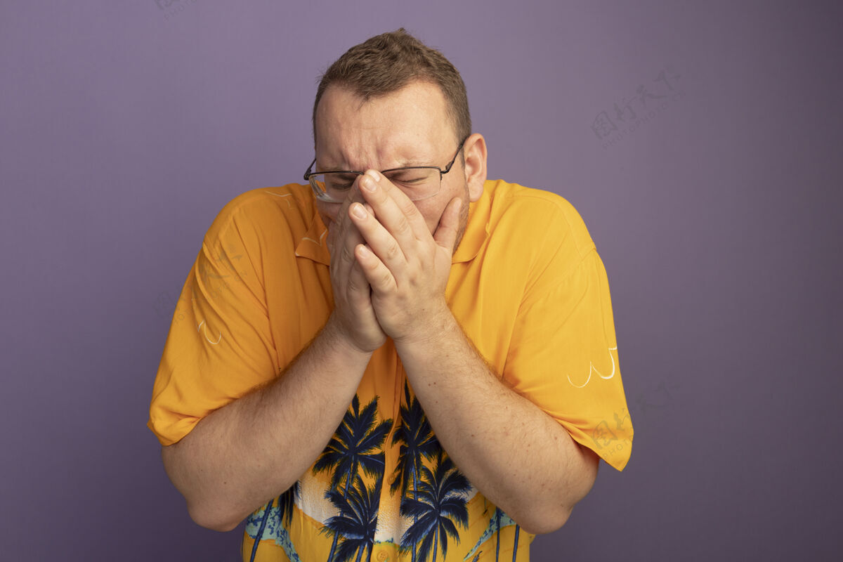 抱着一个戴着眼镜 穿着橙色衬衫的男人手挽手捂着脸 站在紫色的墙上很沮丧男人沮丧脸