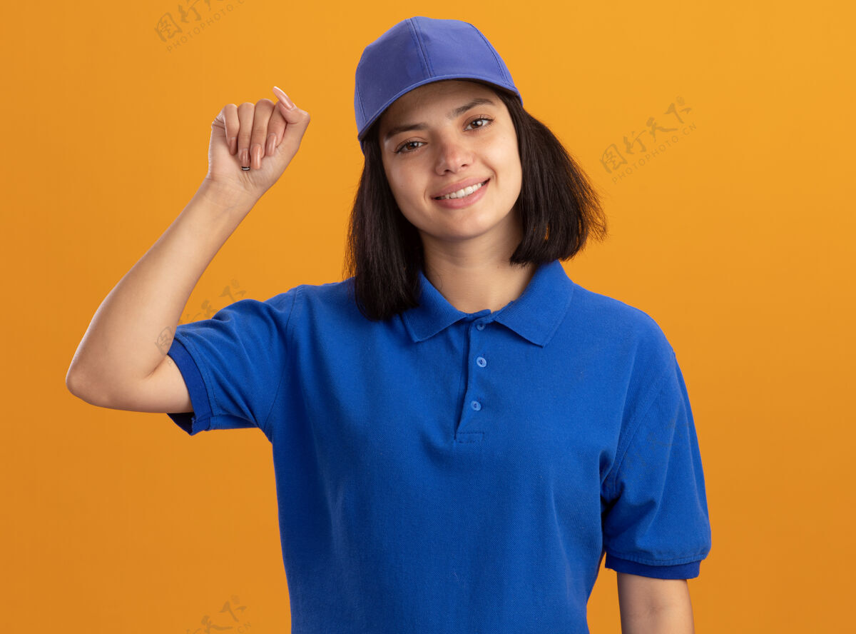 年轻身着蓝色制服 握紧帽子 微笑着站在橙色墙壁上的年轻送货女孩微笑帽子制服
