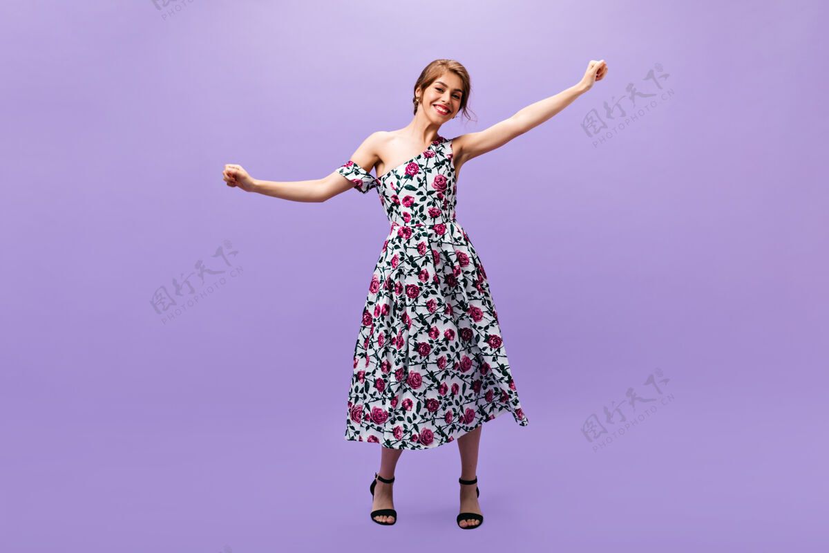 休闲活泼开朗的女孩穿着印花裙在紫色的背景下翩翩起舞可爱漂亮的年轻女子穿着时髦的夏装和黑色高跟鞋有扇子姿势女孩一个
