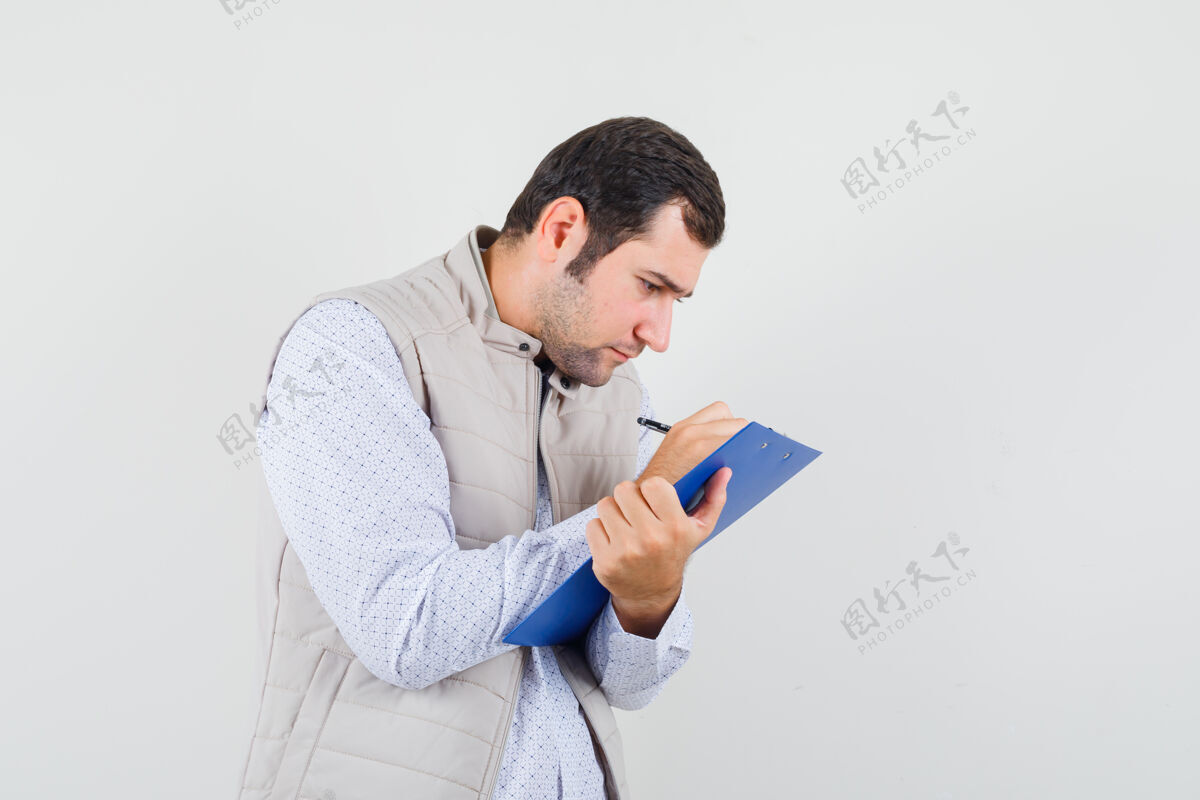 休闲一个穿着米色夹克的年轻人用钢笔在笔记本上写着什么 目光集中 俯瞰前方肖像人焦点