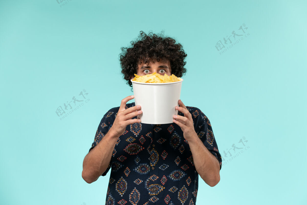 支架正面图年轻人拿着篮子和土豆在蓝色表面cips电影院男年轻人土豆早餐