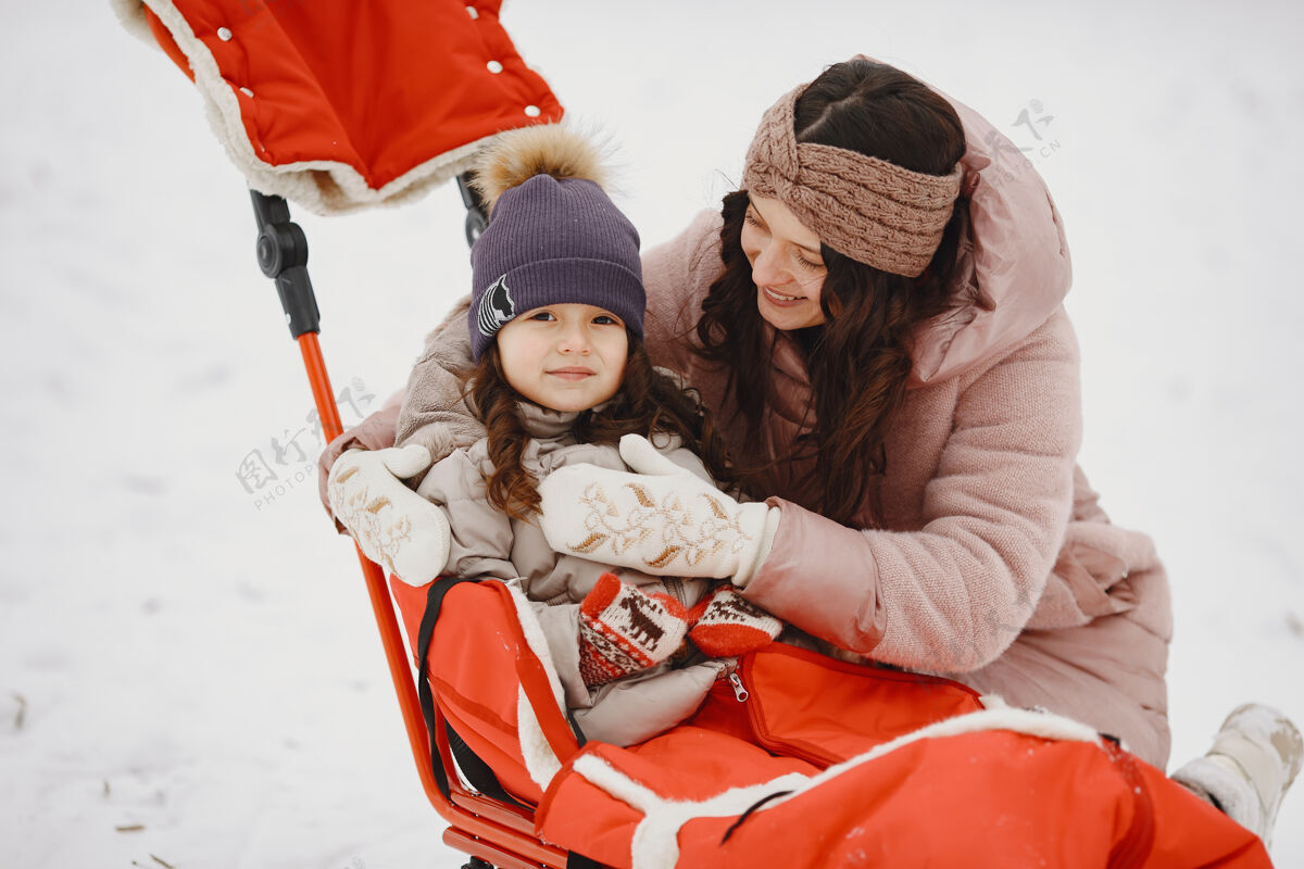 手套带着雪橇的公园里的女人和小女孩孩子童年温暖