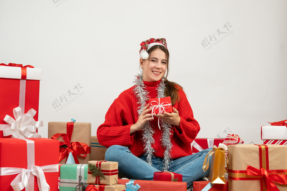 礼物正面图可爱的派对女孩戴着圣诞帽拿着礼物双手围着礼物坐着抱着坐着周围