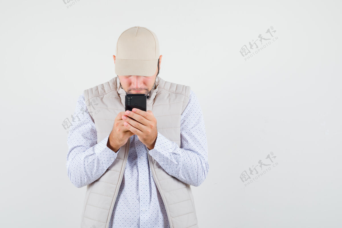 文字年轻人穿着米色夹克 戴着帽子在手机上写短信 看上去很专注前视图夹克姿势自然