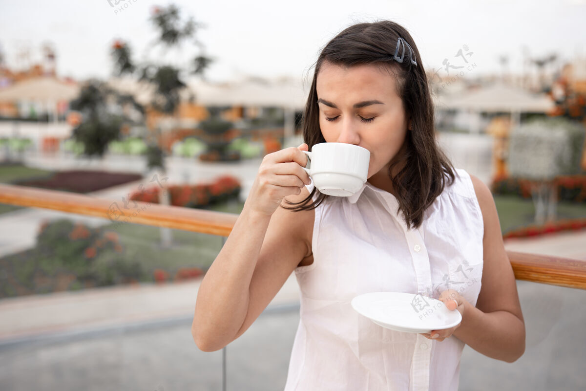 放松迷人的年轻女子 手里拿着一杯咖啡和一个茶托 在户外享受早晨的时光度假和娱乐理念女孩早晨女人