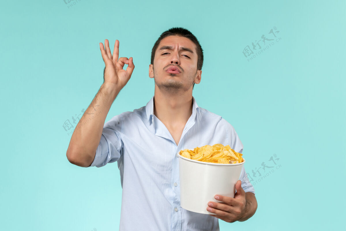 微笑前视图年轻人拿着土豆cips在蓝色的墙上摆姿势孤独遥远的男性电影院电影电影姿势