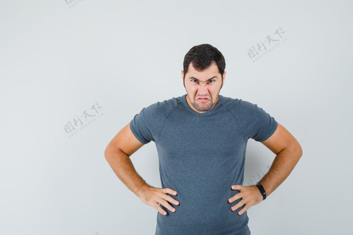 男身穿灰色t恤的年轻男子手挽腰 看上去怒气冲冲隔离男孩电子连接