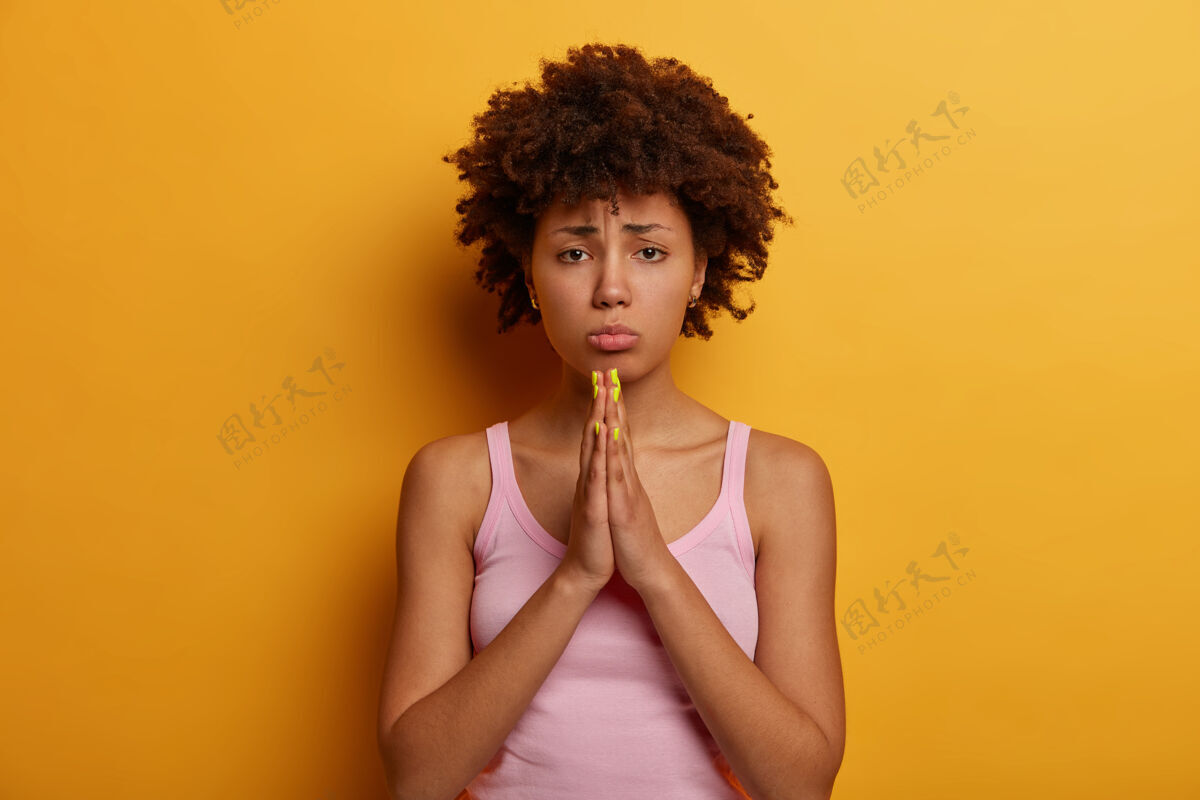 祈祷悲伤的希望的女人乞求你们的帮助 双手合十祈祷 说“请”并请求帮忙 包着嘴唇 穿着休闲装 感觉需要 孤立在黄色的墙上抱歉非洲困难