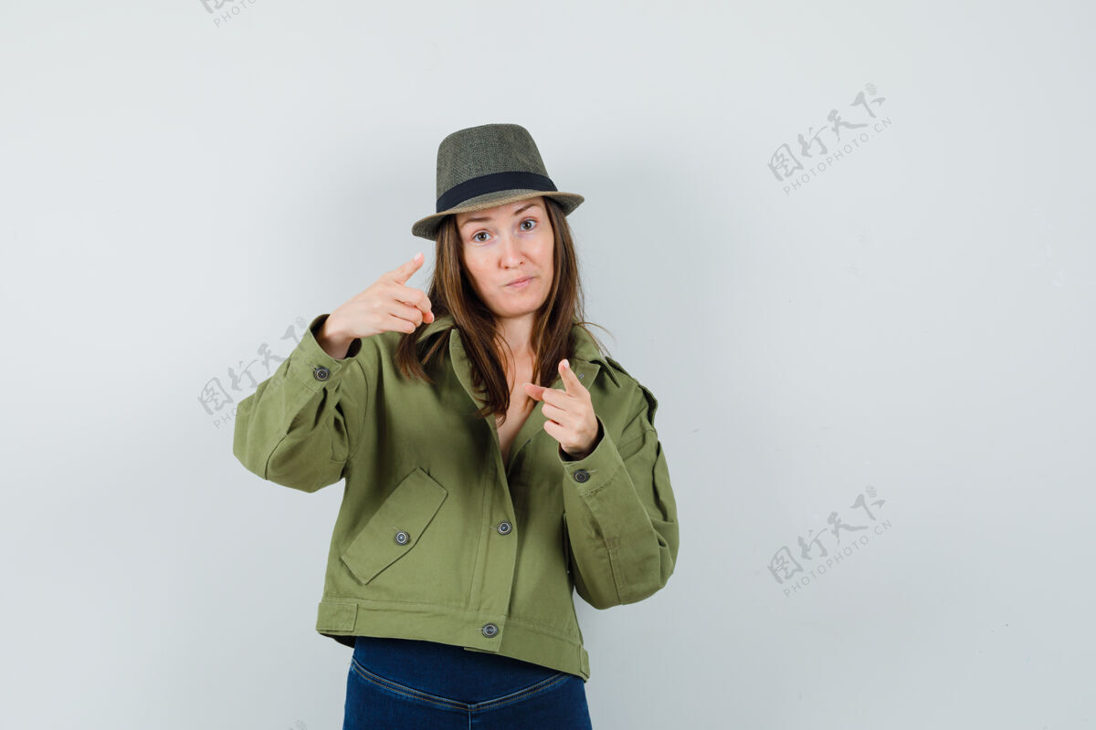 休闲年轻的女士指着摄像机 穿着夹克 戴着裤子 戴着帽子 神情犹豫不决人类黑发优雅