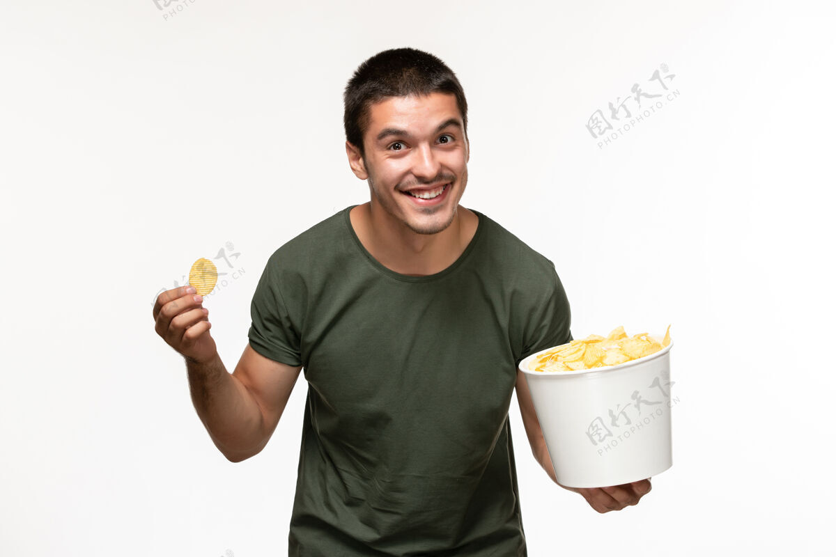电影正面图：穿着绿色t恤的年轻男性 带土豆cips 坐在白色办公桌上吃饭 孤独的电影电影院土豆肖像成人