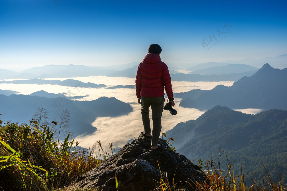人摄影师手持相机 站在大自然的岩石顶上旅游理念工作三脚架雾