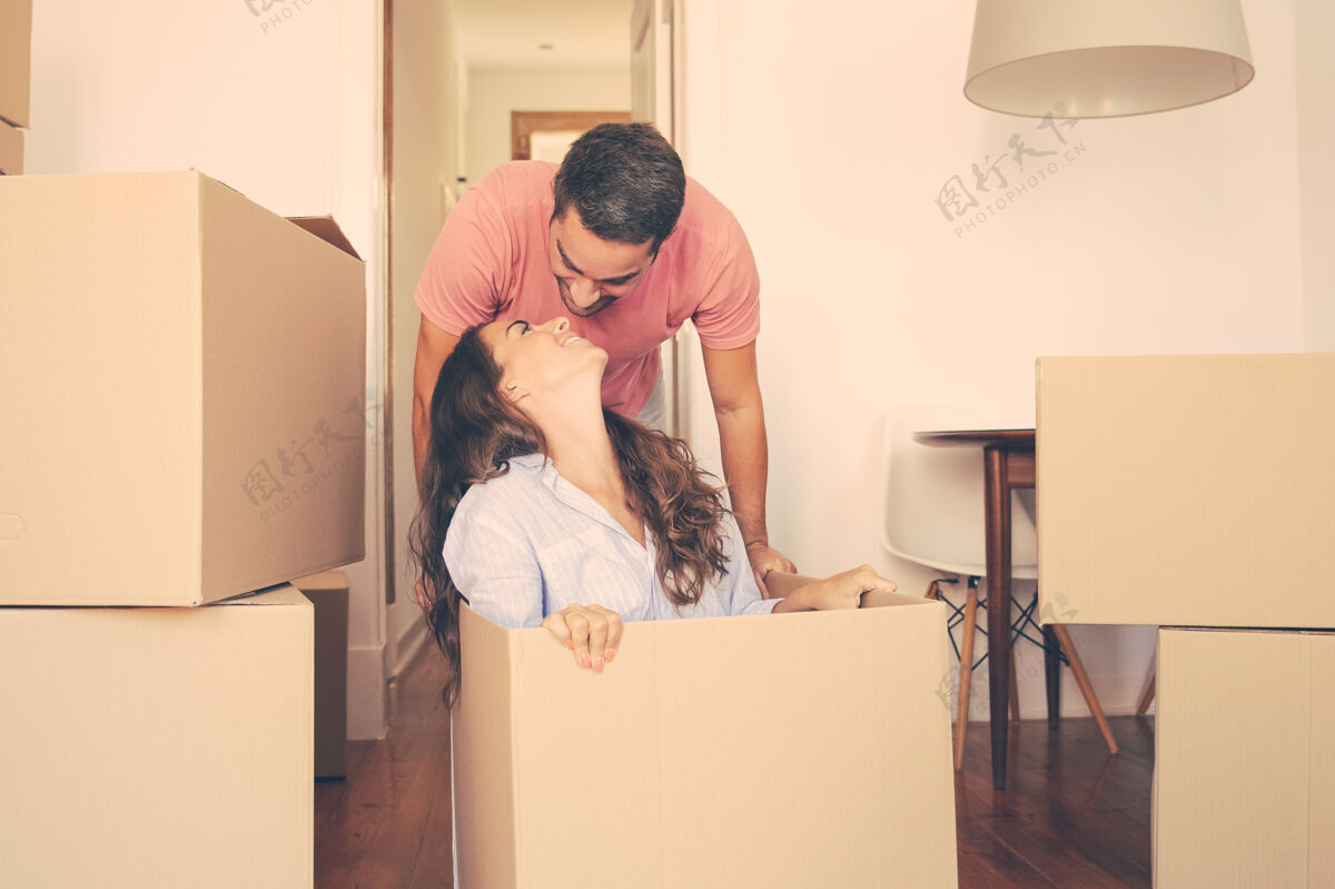 一起一个快乐的年轻人拖着盒子和他的女朋友在里面亲吻她高加索西班牙裔公寓