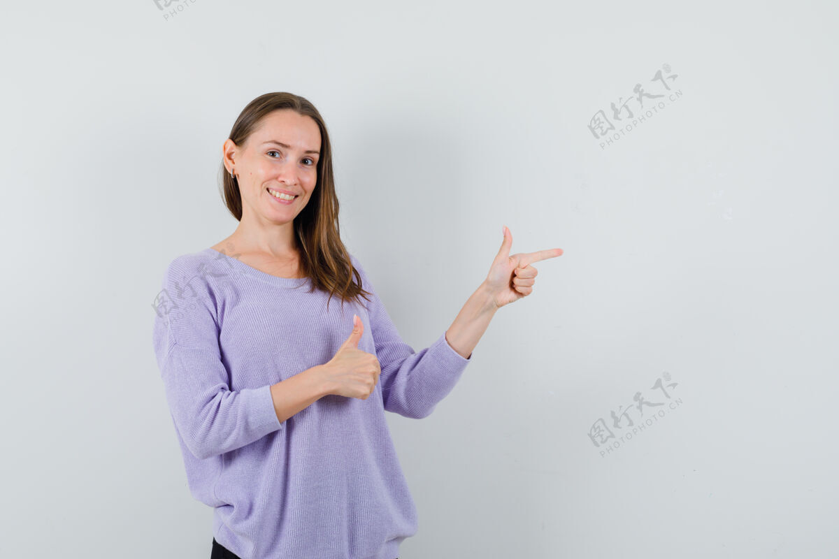 漂亮一位年轻的女性 穿着淡紫色的衬衫 一边指着一边 一边向上竖起大拇指 正面看去卷曲自信女士