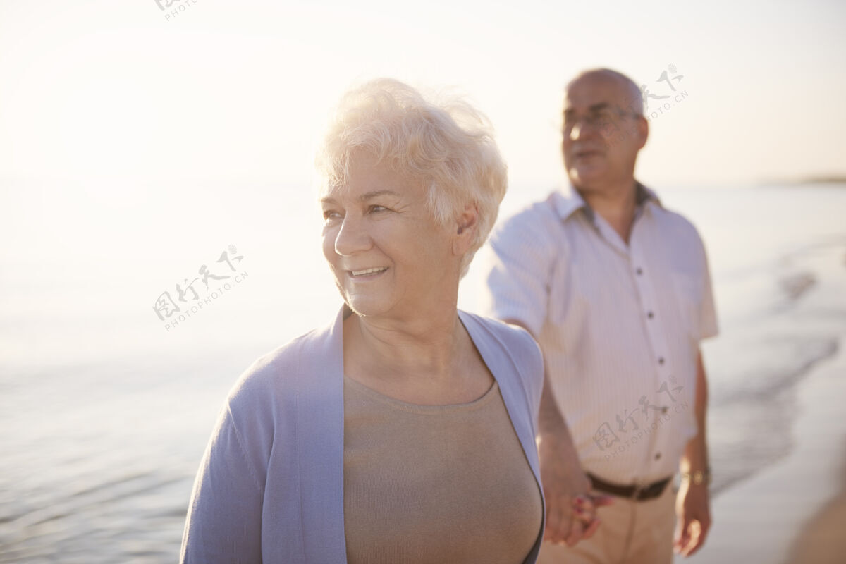 照明老年夫妇在沙滩 退休和暑假的概念爱人欢乐快乐