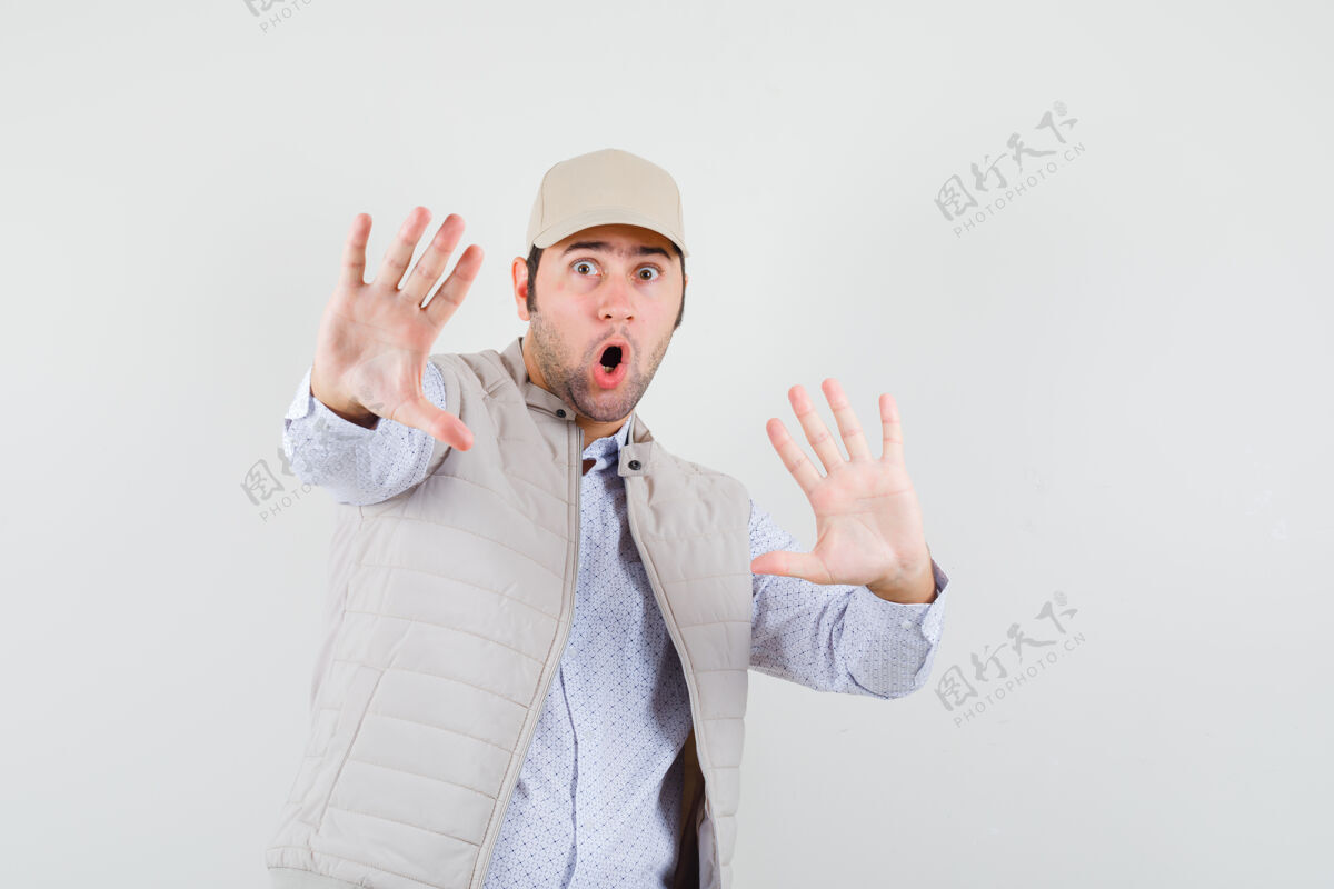 男性身穿米色夹克和帽子的年轻人双手举着停车标志 脸上露出惊讶的表情 正对着前方肖像模型惊喜