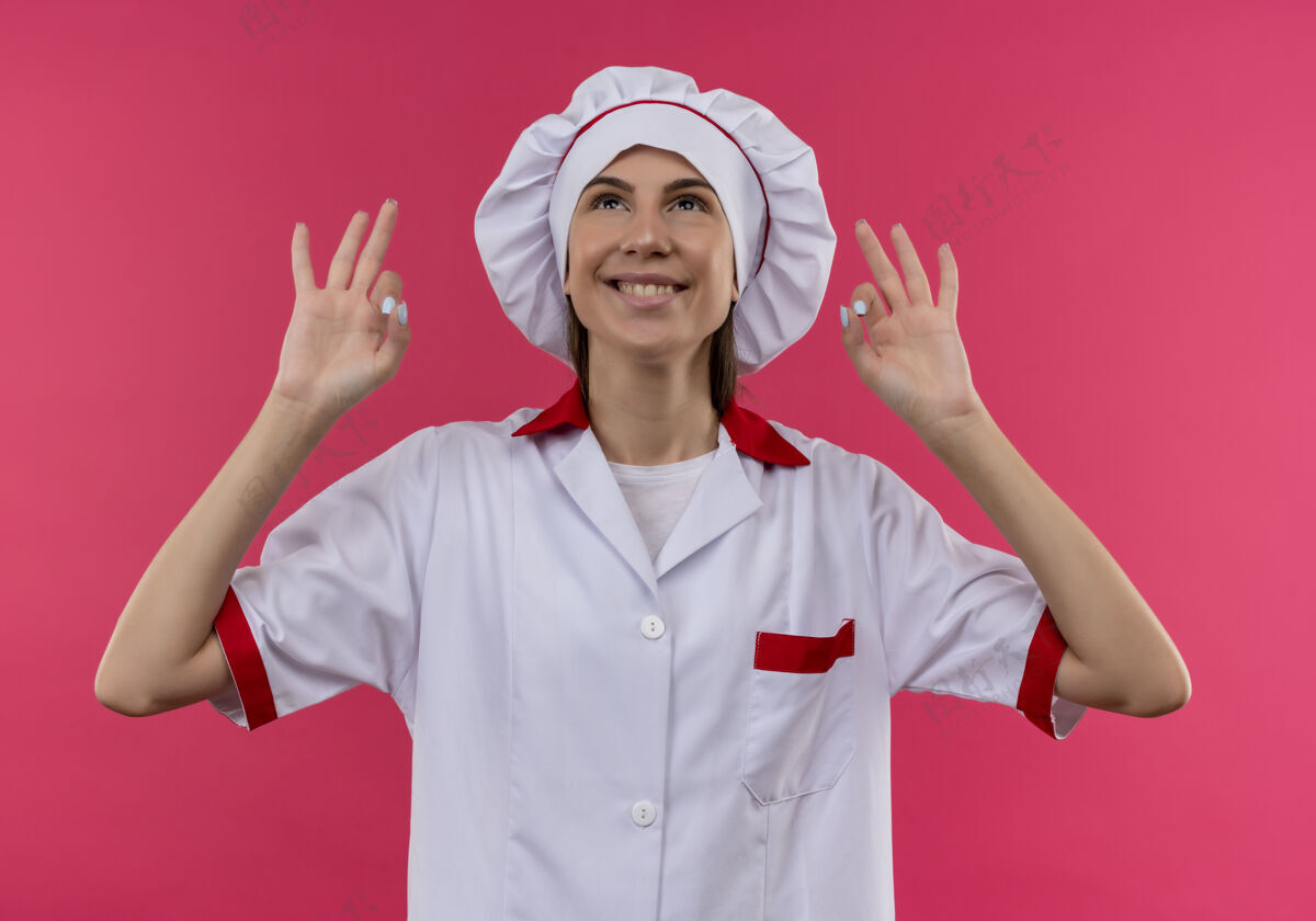 好身着厨师制服 面带微笑的白人年轻厨师女孩摆出良好的姿势 抬起头看着粉色的复制空间粉红微笑制服