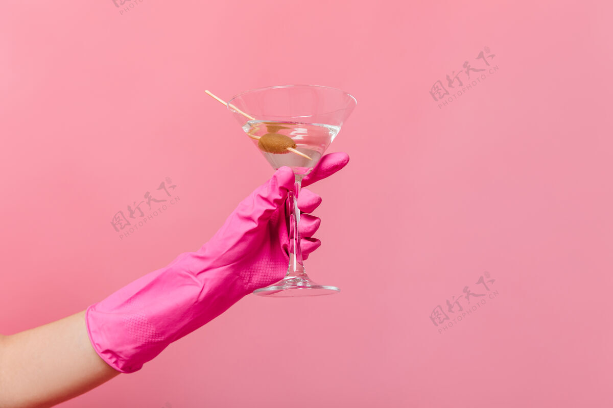 家庭主妇粉红色墙上戴着橡胶手套的手拿着马提尼杯快乐浴袍人
