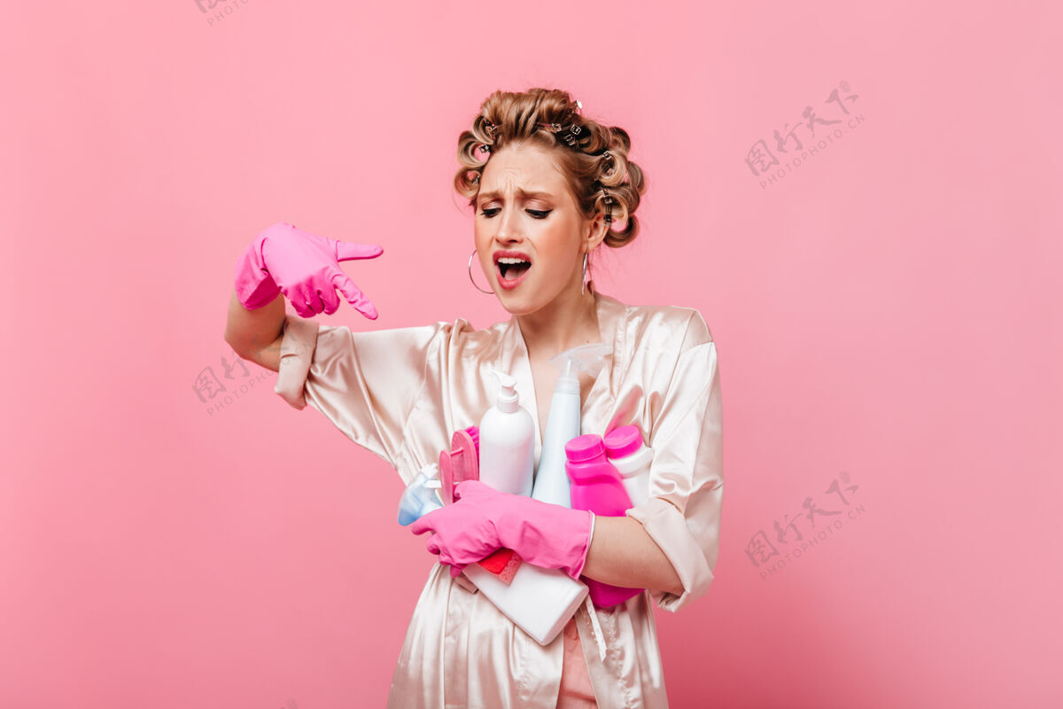人不高兴的女人展示在洗涤剂上 在粉红色的墙上摆姿势享受长袍清洁