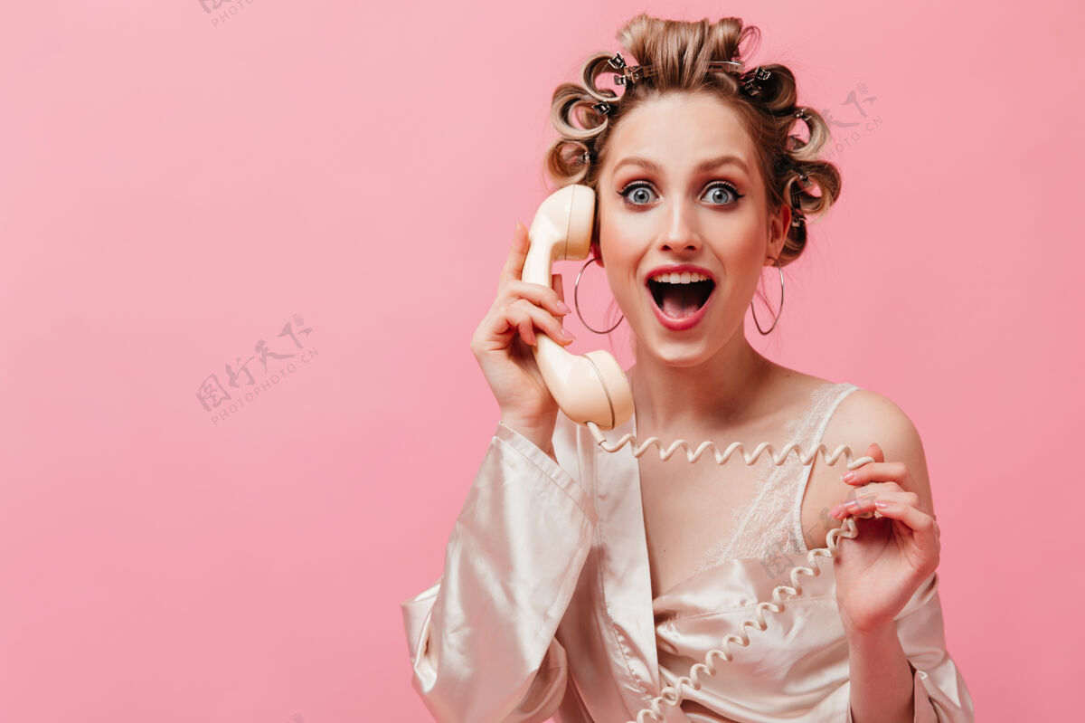 杯子热情的穿着粉色长袍的女人在孤零零的墙上高高兴兴地讲着电话 摆着姿势肖像人可爱