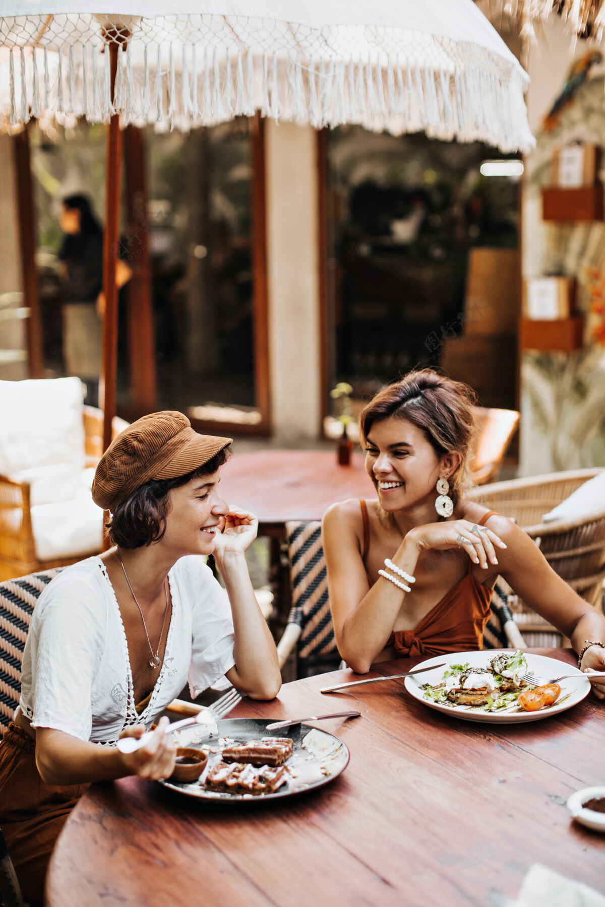 咖啡馆棕色帽子 白色T恤的黑发女人和穿着时髦上衣的朋友微笑着在街边咖啡馆休息朋友热女士