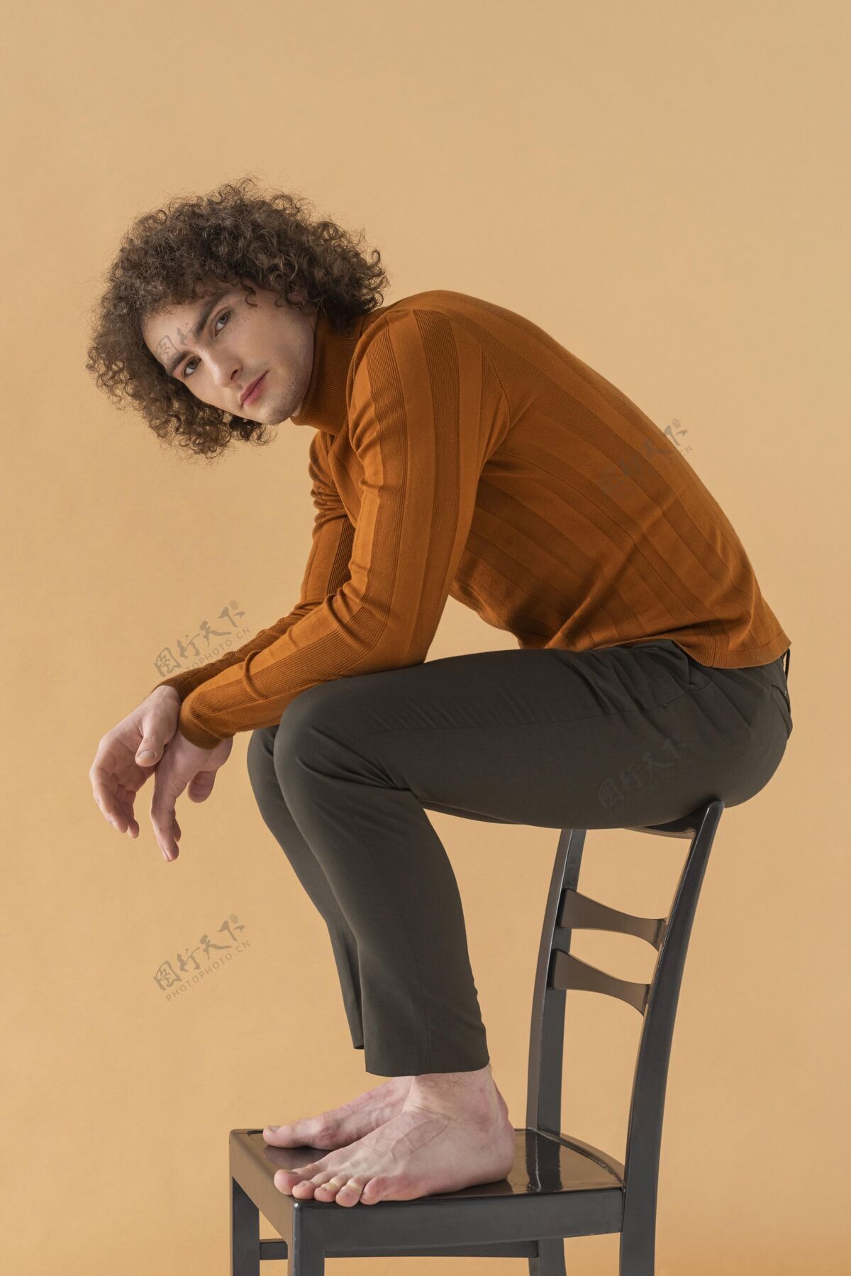 年轻卷发男人穿着棕色衬衫在椅子上摆姿势椅子姿势模特