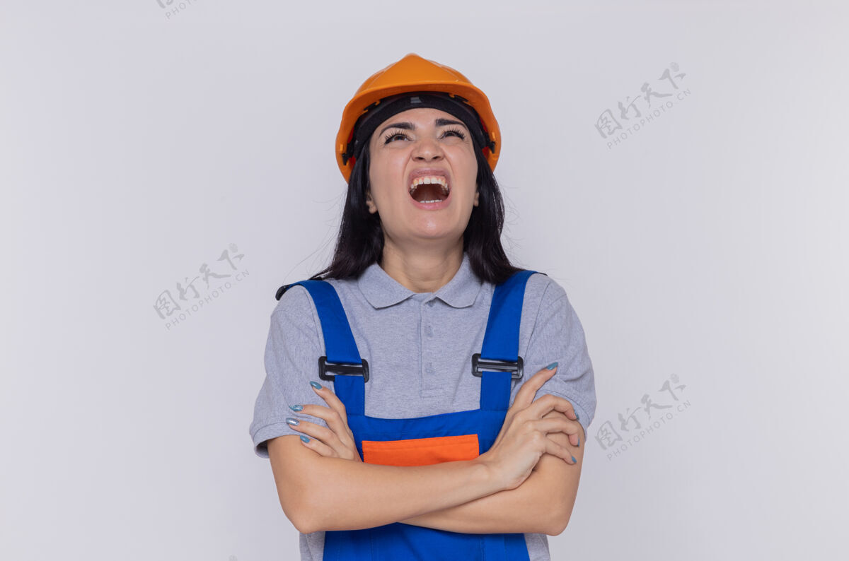 建设者身穿施工制服 头戴安全帽的年轻建筑工人站在白墙上 抬头高喊着 表情咄咄逼人头盔站着喊叫