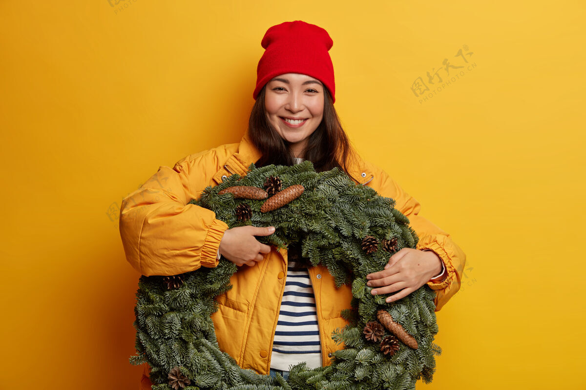 夹克年轻漂亮的女人拿着圣诞装饰品满意快乐花环