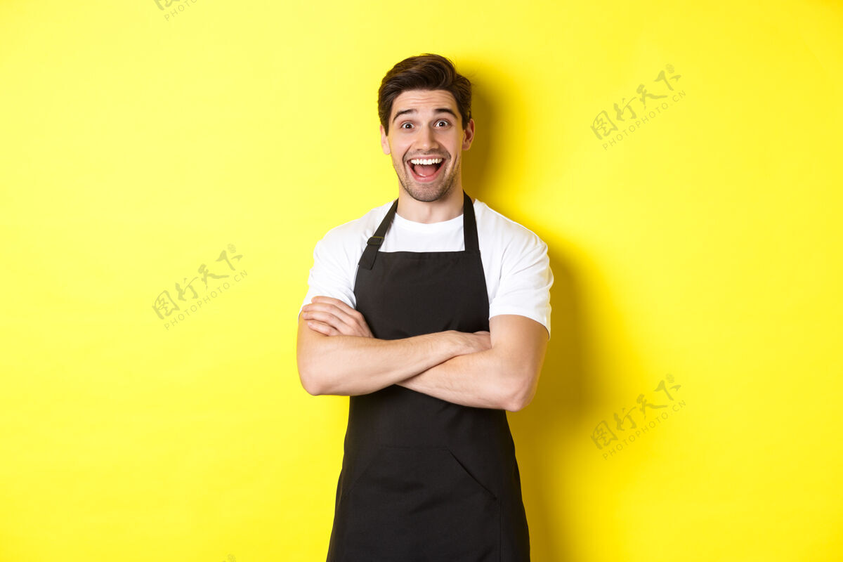 烹饪穿着黑色围裙的帅哥咖啡师惊讶地扬起眉毛 站在黄色的背景下 显得很惊讶工作室自信模特