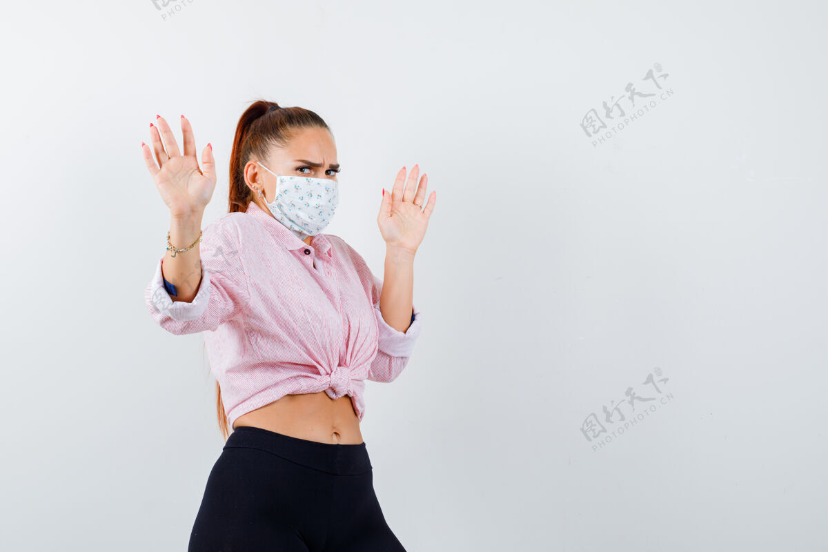 面具穿着衬衫 裤子 戴着医用面罩 脸上露出手掌投降的年轻女性正视图人物衬衫惊喜