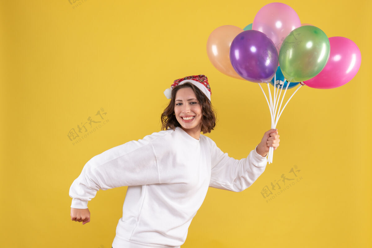 成人正面图年轻漂亮的女性手持五颜六色的气球在黄色的新年情感女人彩色圣诞情感颜色正面