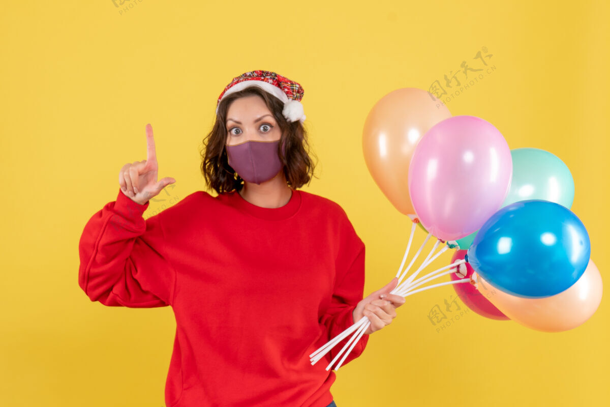 面具正面图：戴着面具手持气球的年轻女子在黄色病毒冠状病毒派对上感慨新年彩民外科面具正面情感