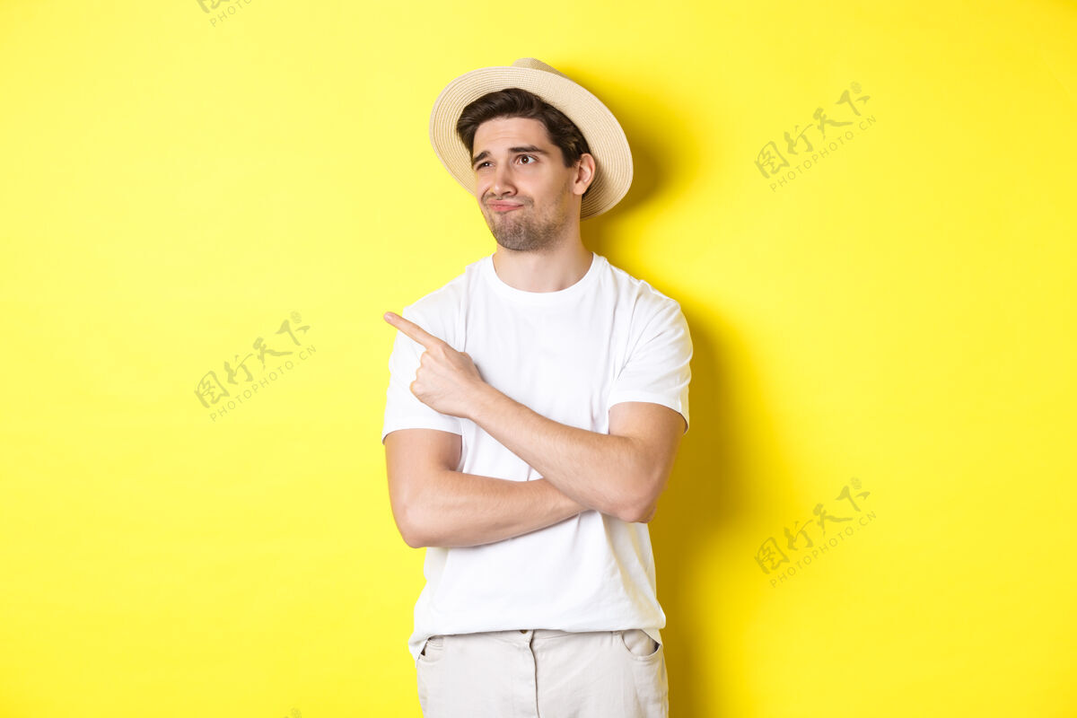 自信旅游和生活方式的概念不满的男性游客抱怨 失望地看着左上角的宣传片 站在黄色背景下时尚帽子夏天