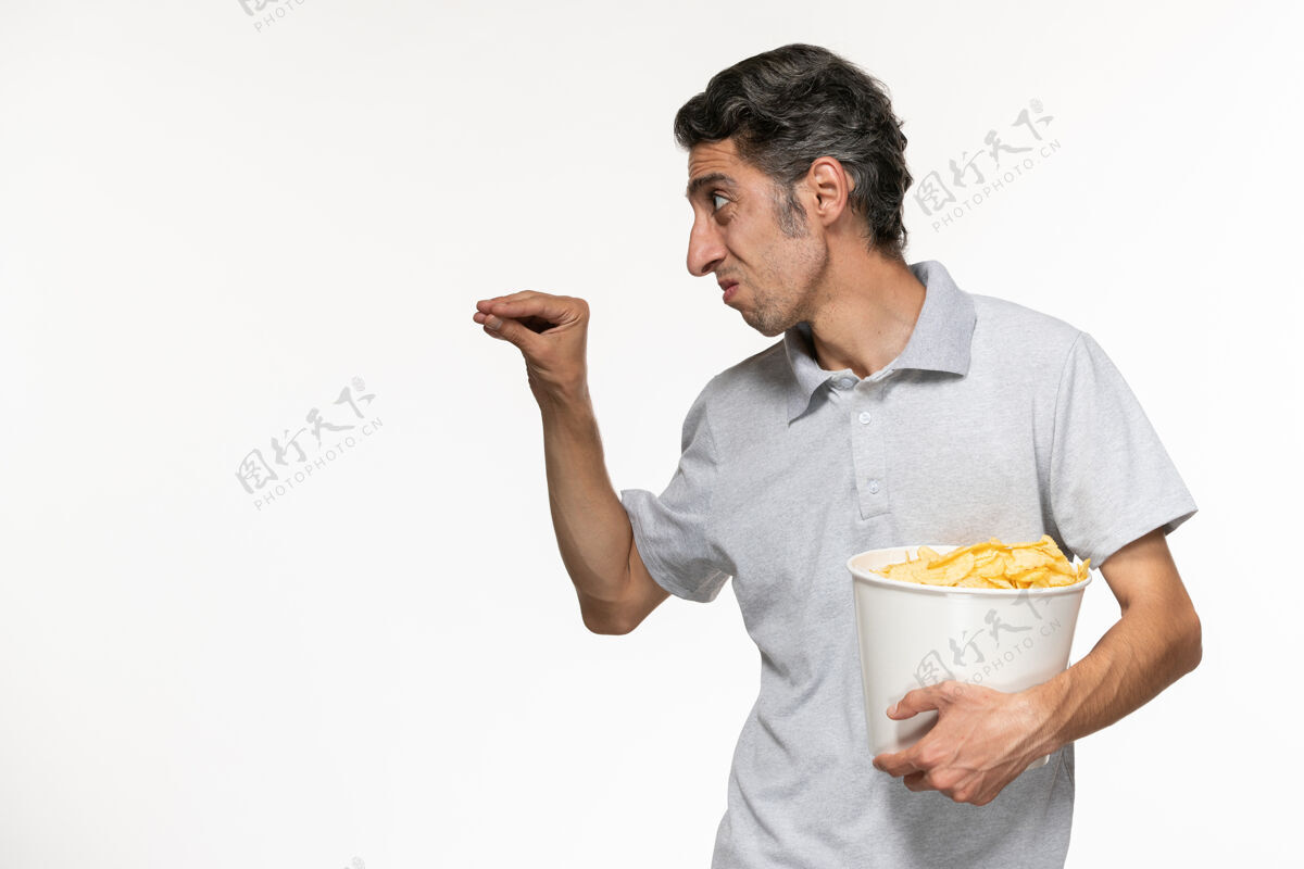 电影院正面图：年轻的男性拿着一个篮子 里面放着薯片 和一个在白色表面上的人说话前面远程男