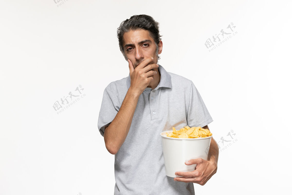 篮子正面图年轻男子抱着篮子 在白色地板上放着薯片 男人在遥远的电影院里孤独地看电影前面孤独土豆